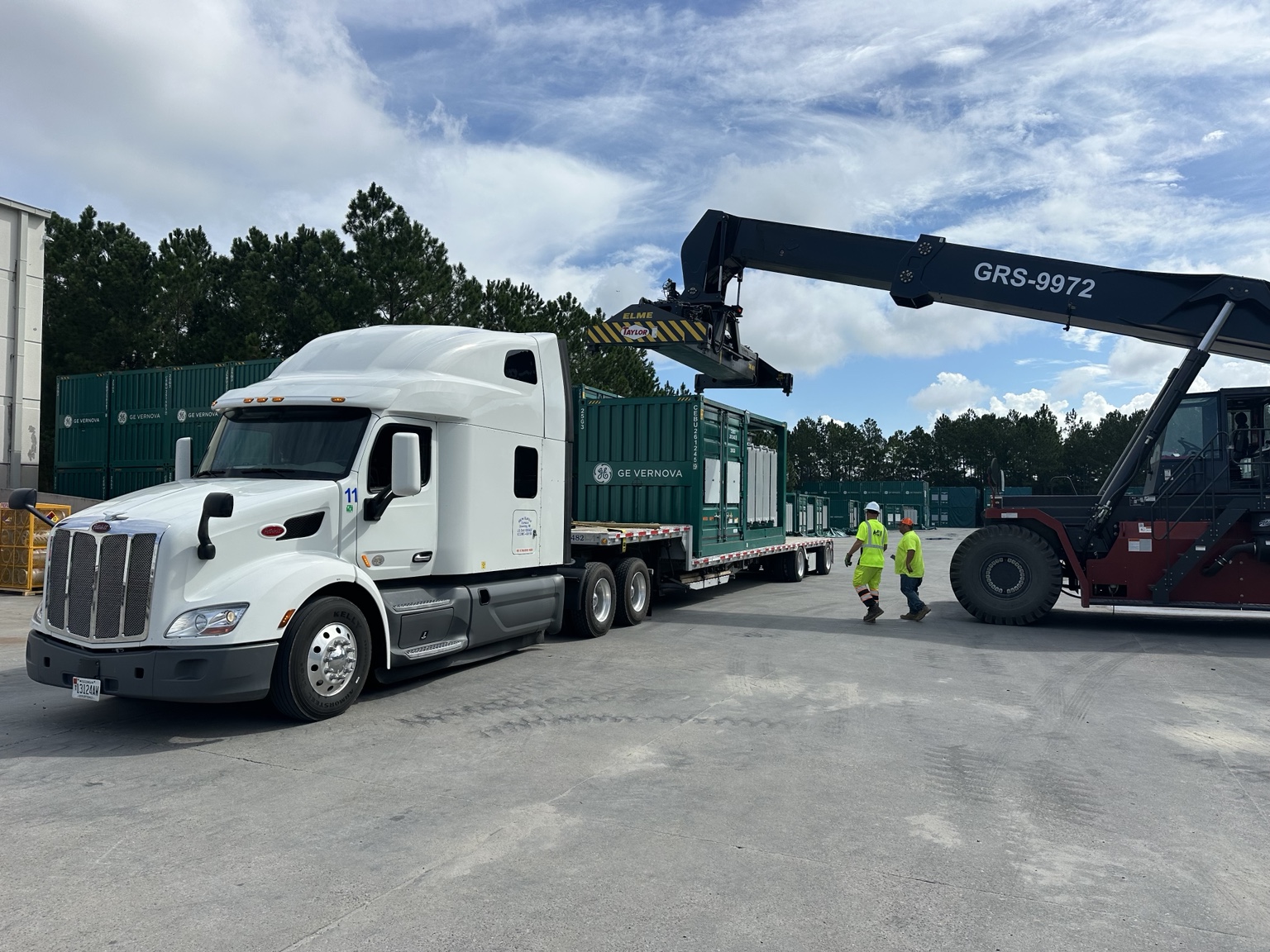 New Haven Express’s white Peterbilt and step deck trailer carrying containerized equipment at a loading yard